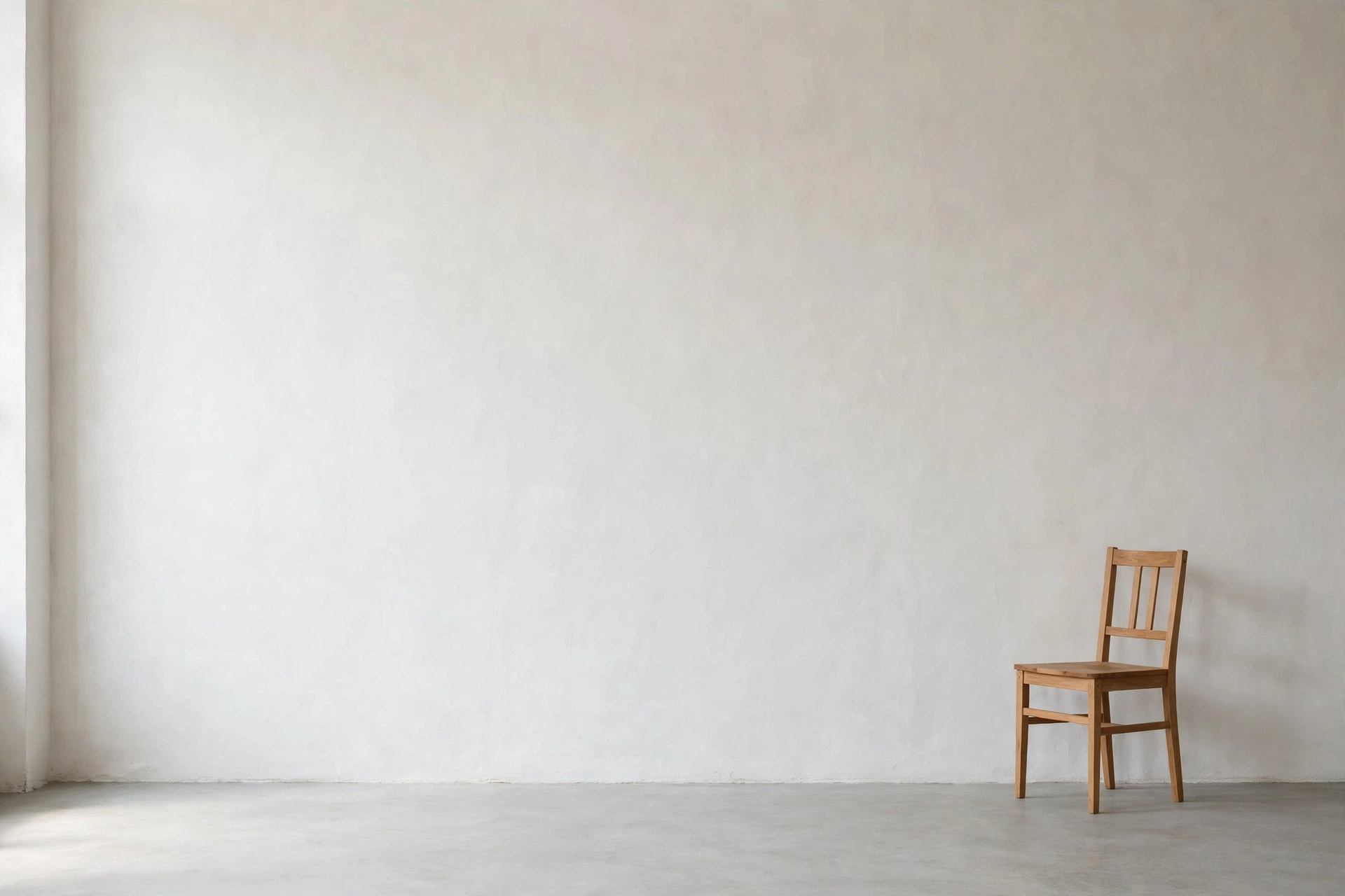 Empty calm wall with generous negative space beside a single chair in a minimalist studio